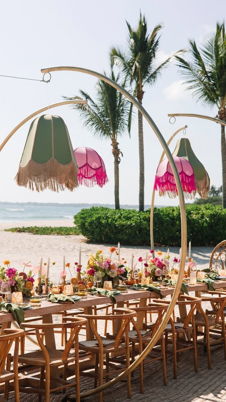 Vibrant wedding table setting with colorful flowers and fringed lampshades on a beach.
