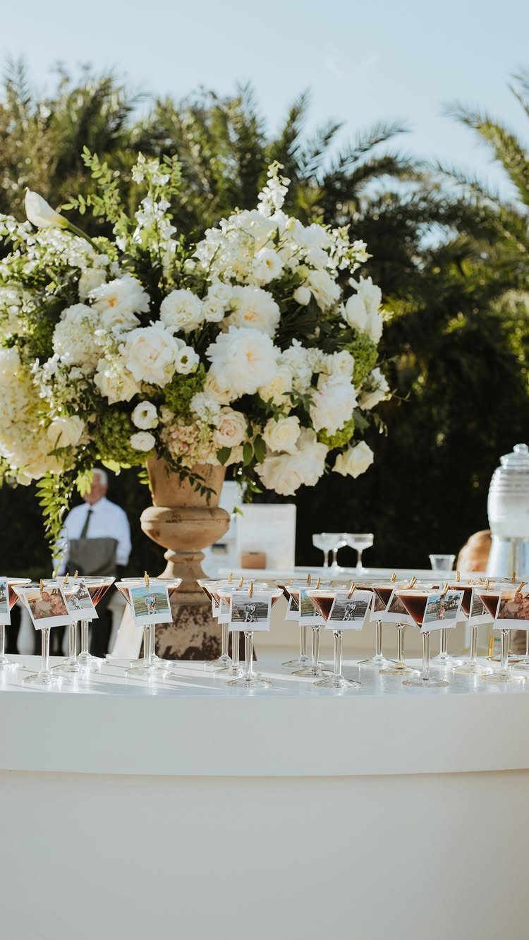 White floral arrangement and colorful cocktails with photo cards on a white bar