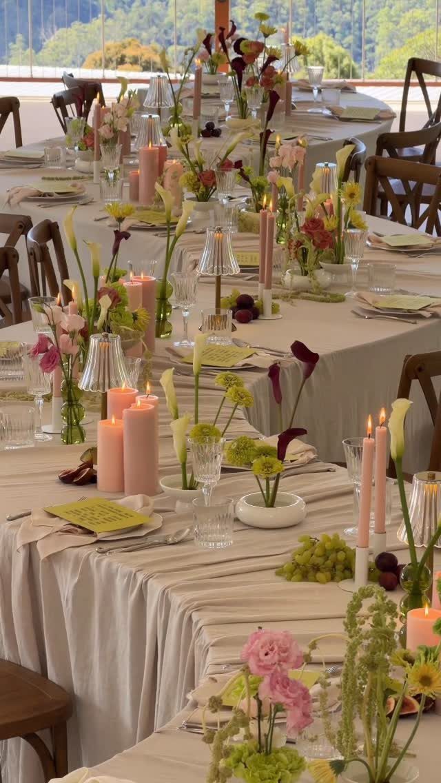 Long dining tables with beige linens, pink candles, and diverse floral arrangements.