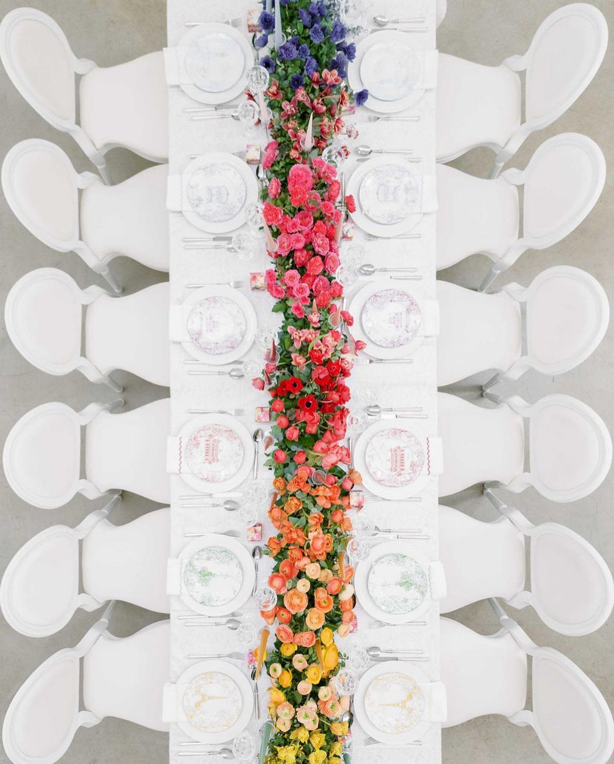 Long white wedding table with a vibrant rainbow floral runner and white chairs.