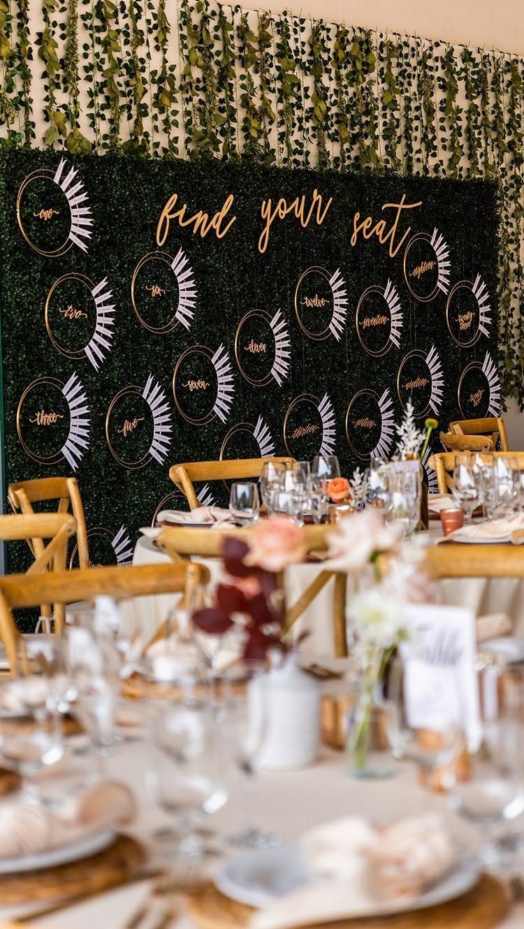 Wedding seating chart on a green hedge wall with wooden chairs and tables.