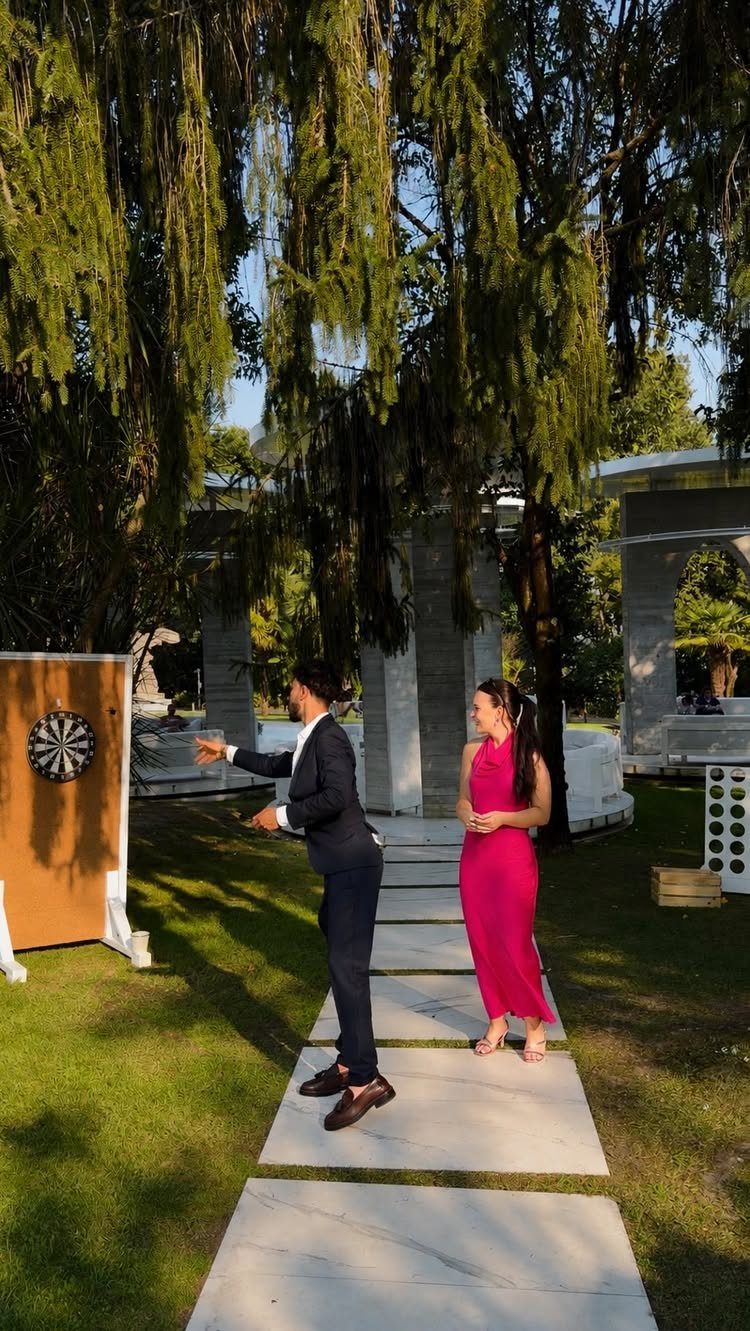 Man in suit playing darts with a woman in pink dress outdoors.