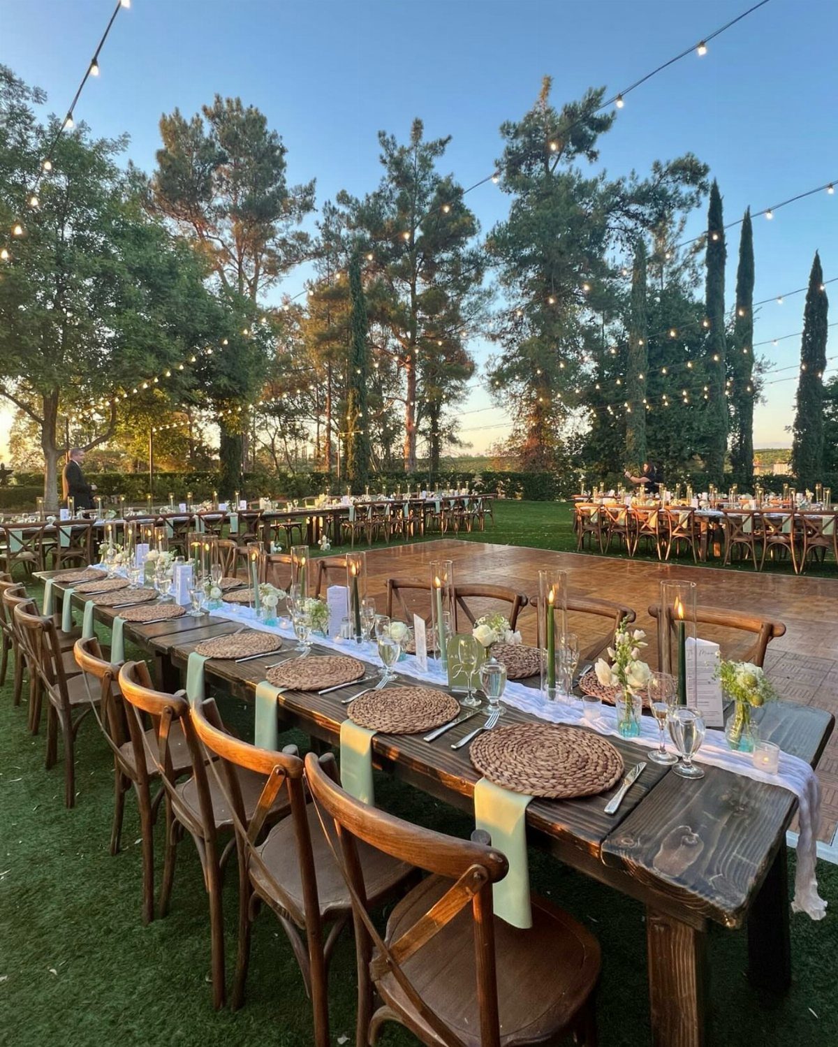 Long wooden banquet table with rustic decor and cross-back chairs in outdoor setting