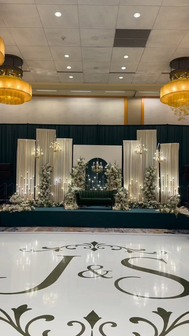 Wedding reception stage with white drapes, floral arrangements, and a monogrammed dance floor.