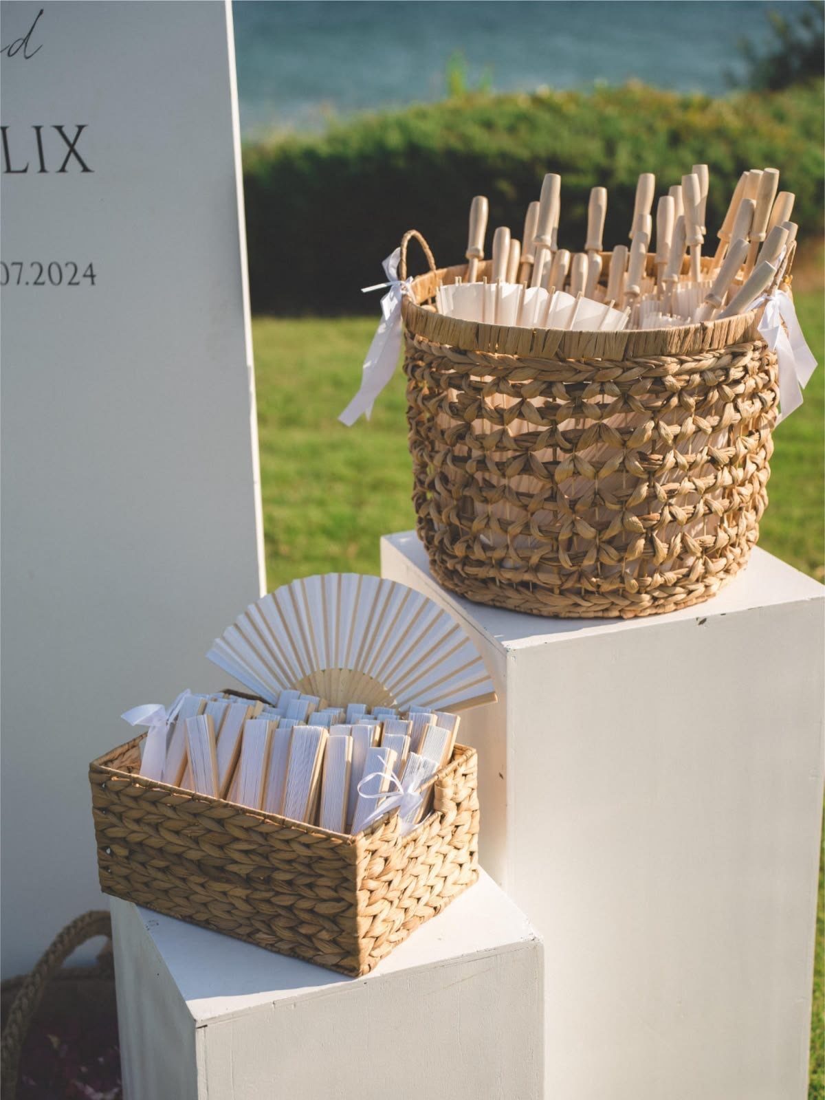Woven baskets with white fans and favors on white pedestals next to a sign.