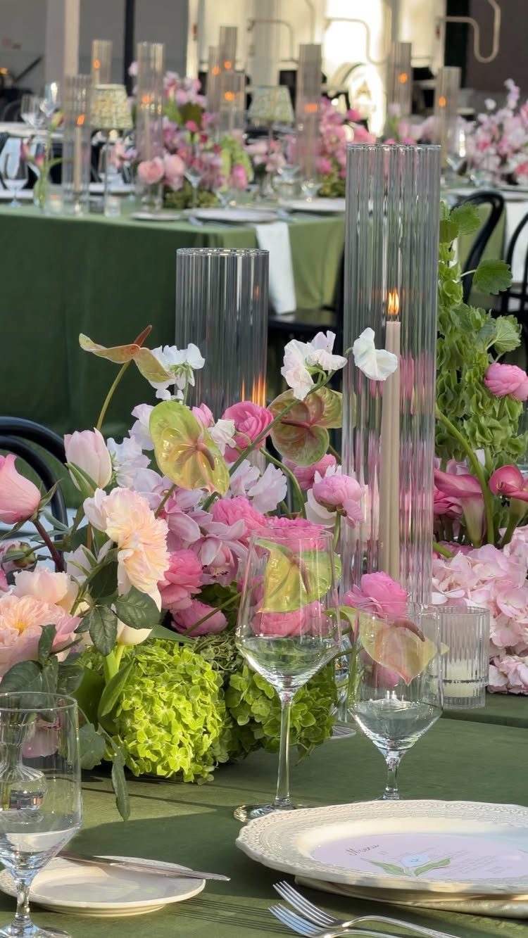 Pink and green floral centerpieces with tall ribbed glass candle holders on green tablecloth.