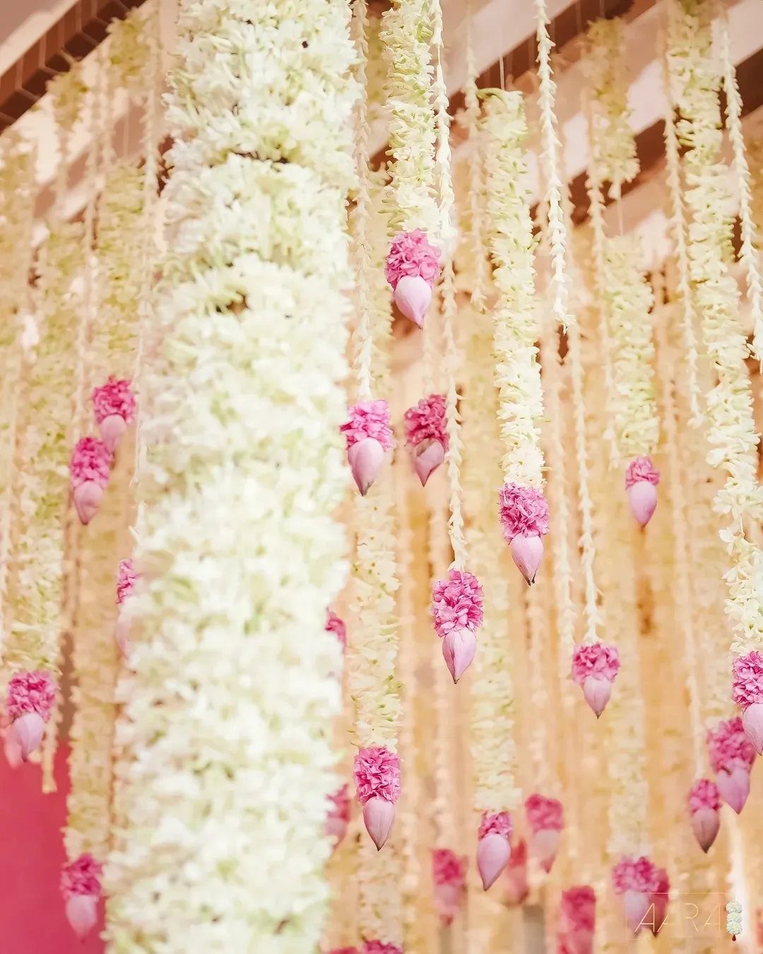 Hanging white flower garlands and pink lotus buds as wedding reception decorations.