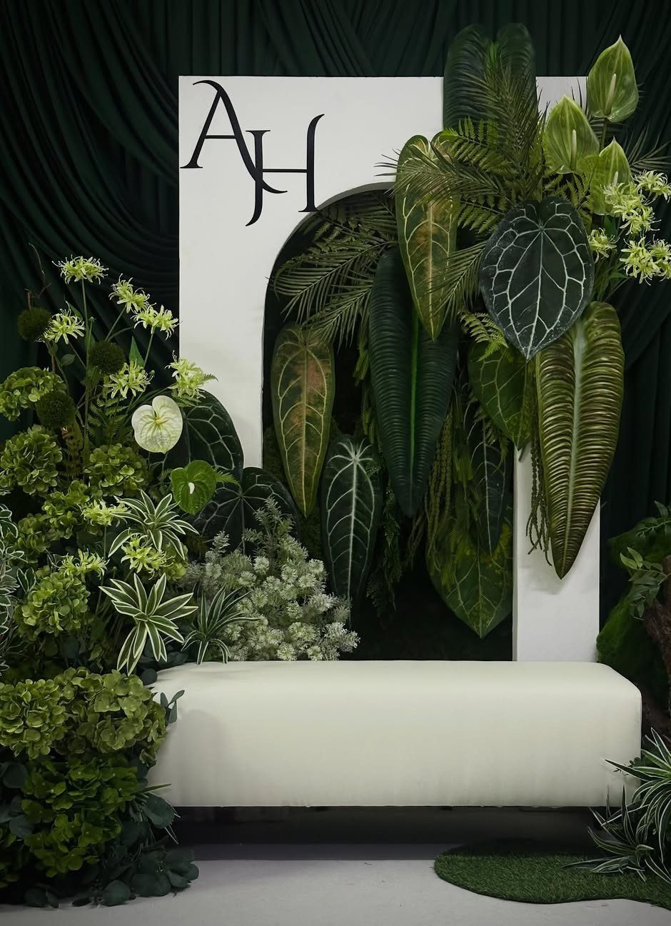 Tropical green foliage and white flowers surrounding a white bench and arched backdrop.